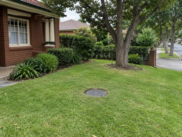 Grass front yard with a round capped inspection cover near a brick house in Normanhurst